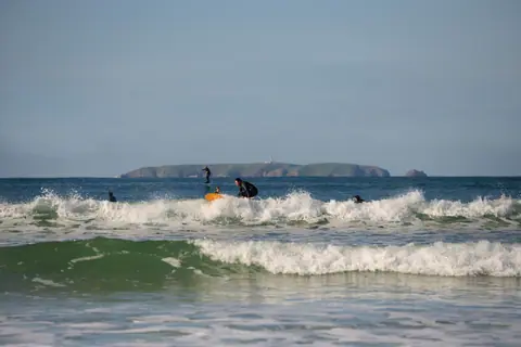 Group of surfers negotiating waves at a sunny beach, perfect for surf enthusiasts.