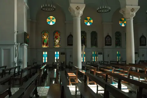 Sunlit church interior with stunning stained glass windows and wooden pews.