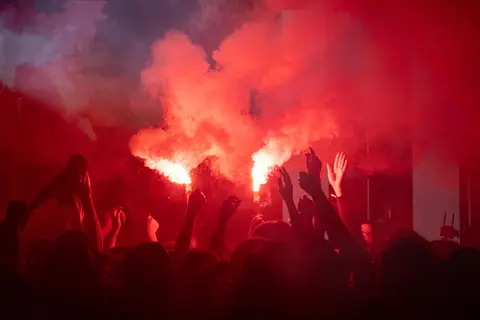 Vibrant scene of a lively crowd celebrating with red flares at night.