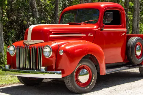 Classic red Ford truck from the 1940s featuring iconic design, parked in nature.