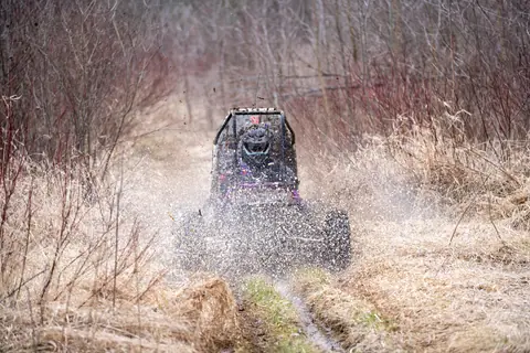 All-terrain vehicle splashing through mud on a forest trail during an adventure ride.