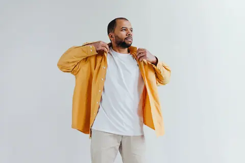 Fashionable man wearing a yellow shirt and white t-shirt against a minimalistic white backdrop.