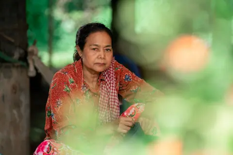 Portrait of a woman in colorful attire sitting thoughtfully indoors with a blurred foreground.