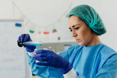 Focused female scientist in lab gear performing liquid analysis experiment.