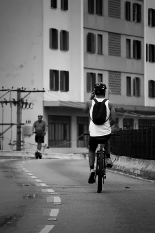 Monochrome photo of a cyclist and runner on an urban street, showcasing dynamic movement.