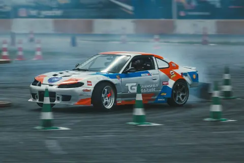 Action-packed scene of a customized car drifting around cones on a race track.