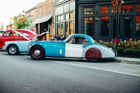 A vibrant scene of classic cars parked on a charming city street during the day.