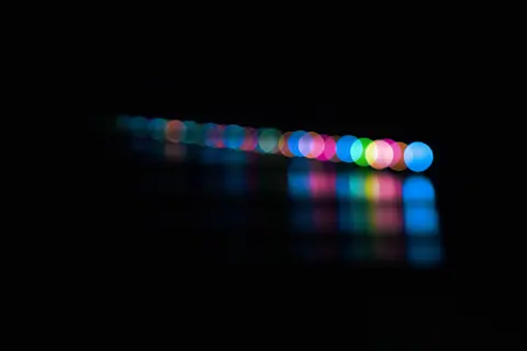 Colorful bokeh balls in a line, creating a vibrant abstract pattern against a dark backdrop.