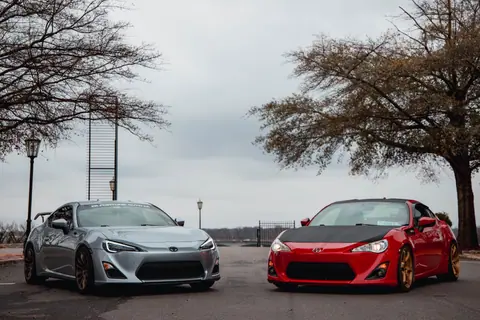 Two sports cars parked under cloudy sky, showcasing luxury and power.
