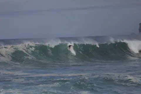 A surfer rides an enormous wave, showcasing the thrill of surfing in rough seas.