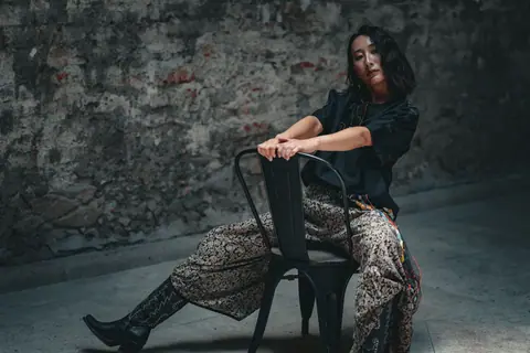 Fashionable woman in a moody, urban setting sitting on a metal chair.