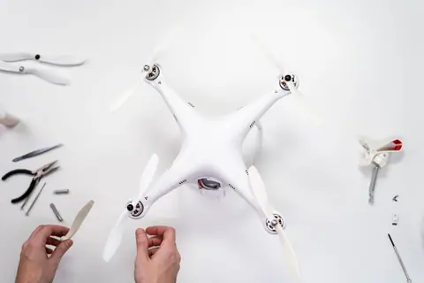 Hands assembling a quadcopter drone on a white surface with various tools around.