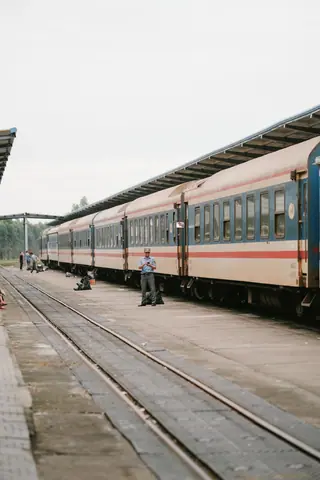 A serene scene of a passenger train waiting at an outdoor railway platform with one person visible.