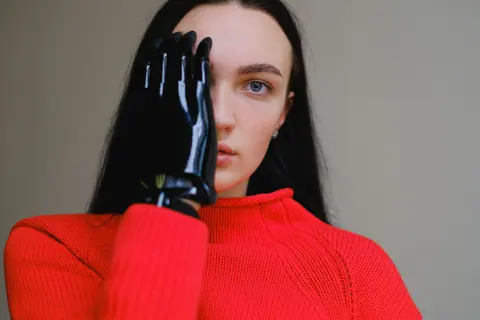 Portrait of a woman with a bionic prosthetic hand wearing a vibrant red sweater.