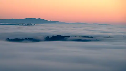 A tranquil mountain landscape covered in soft clouds at sunrise.