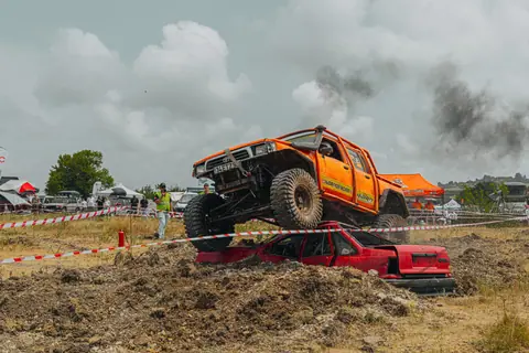 Orange offroad truck crushing a red car in an outdoor auto racing event.