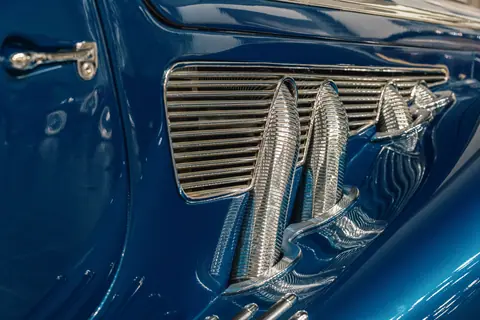Detailed view of a vintage blue car's chrome exhaust and grill.