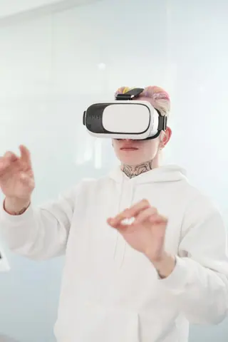 A young adult in a white hoodie immersed in a virtual reality experience with VR goggles.