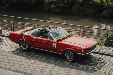 A vintage red Ford Mustang convertible decorated for a wedding, parked by a serene canal.