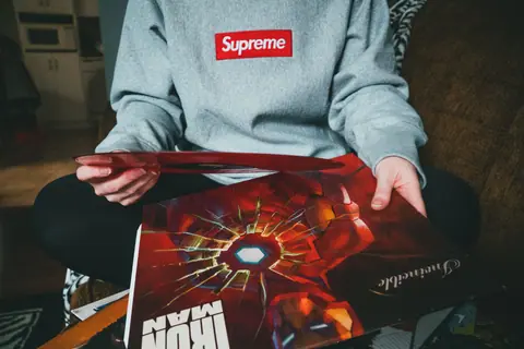 Crop unrecognizable person in gray hoodie sitting with crossed legs on sofa and demonstrating red vinyl record in room
