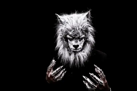 Striking portrait of an adult in a realistic werewolf costume with metallic claws against a black background.