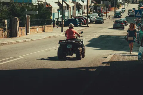 A person rides a quad bike through a busy urban street during the day.