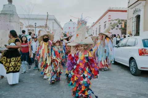 Vibrant traditional parade with participants in colorful costumes on a street in Oaxaca, Mexico.
