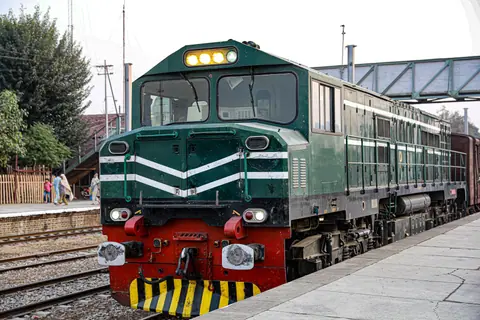 A green locomotive arrives at an outdoor train station with passengers nearby.