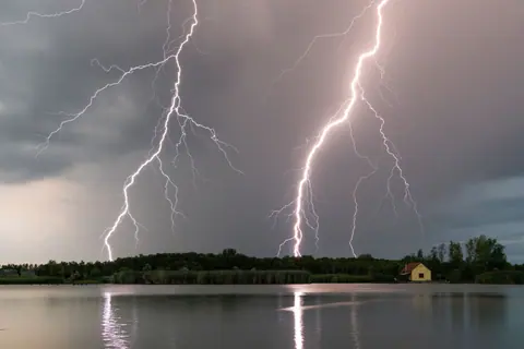 Stunning capture of multiple lightning bolts striking over a calm lake during a thunderstorm at twilight.