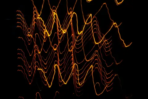 Long exposure of creative modern freezelight light painting with bright wavy lines creating patterns shining on black background in darkness