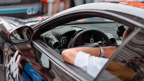 Close-up view of a luxury car interior with driver at an auto event. Modern dashboard and sleek design.