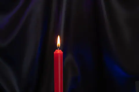 A serene image of a red candle burning brightly against a black background, creating a warm and tranquil atmosphere.