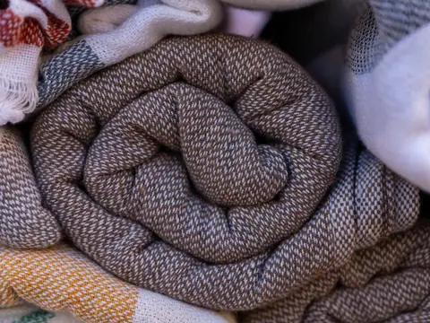 Close-up of neatly rolled fabrics showcasing intricate patterns and cozy textures in neutral tones.