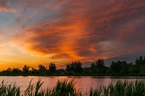 Vibrant sunset over a serene lake with lush greenery and dramatic sky.
