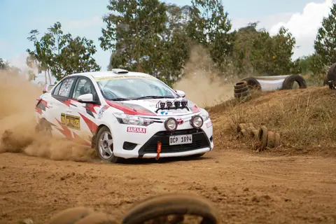 A thrilling image of a rally car drifting on a dirt track, kicking up dust with trees in the background.
