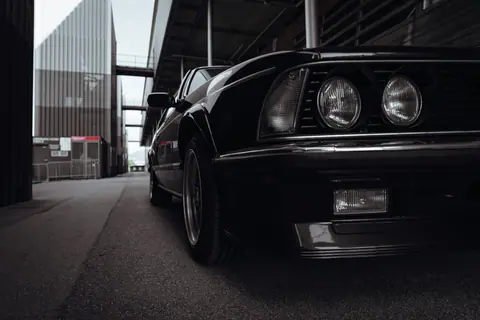 Classic black car with a vintage look parked in an urban industrial area.
