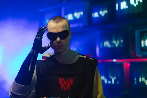 Portrait of an individual in futuristic gear, featuring a prosthetic arm and sunglasses.