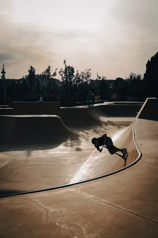 A skateboarder performs a trick in an urban skatepark at sunset, capturing dynamic motion and moody lighting.