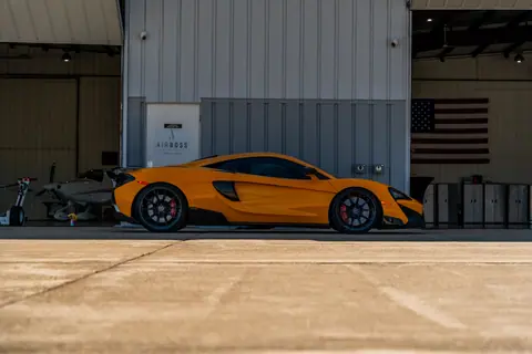 Sleek orange McLaren parked at an airport hangar in Illinois with an American flag in the background.