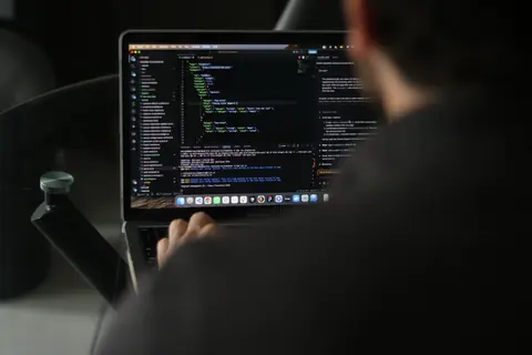 A focused developer writing code on a laptop in an indoor workspace.