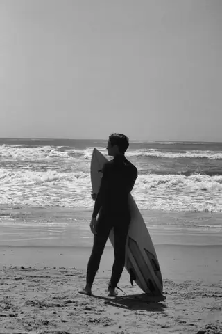 Silhouette of a surfer with a surfboard gazing at the ocean waves on a beach.