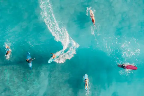Drone shot capturing surfers enjoying vibrant turquoise ocean waves, displaying dynamic water sports action.