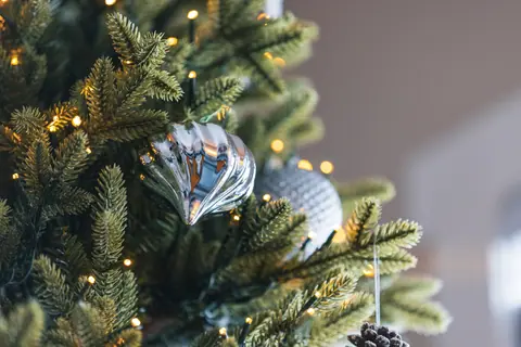 Close-up of a Christmas tree with silver ornaments and pinecone, adorned with twinkling lights.