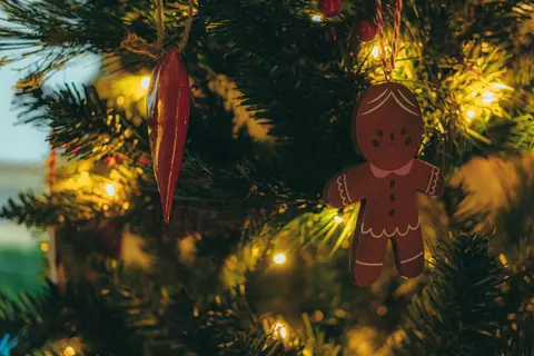 A charming gingerbread man ornament hanging on a decorated Christmas tree with lights.