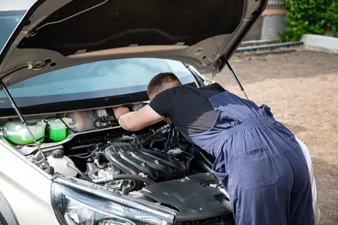 Mechanic repairing car engine in daylight, showcasing technical skills.