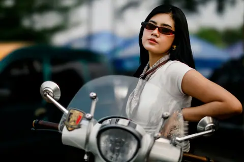 Stylish woman wearing sunglasses poses with a vintage scooter outdoors, creating a chic and modern vibe.
