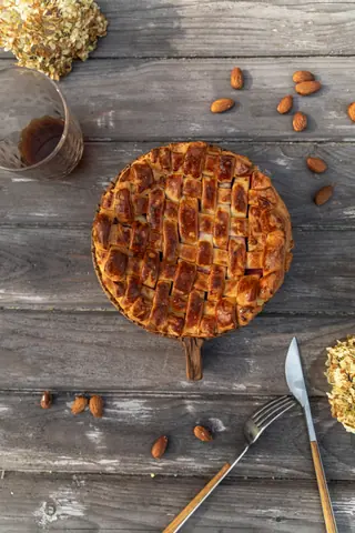 A homemade apple pie with a lattice crust on a rustic wood table, surrounded by almonds.