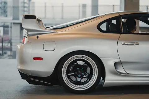 Close-up of a shiny silver Toyota Supra parked outdoors, showcasing sportscar design and side view features.