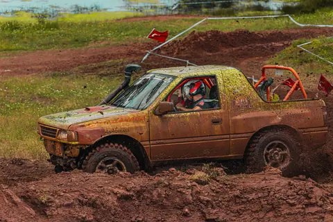 A four-wheel drive vehicle tackles a muddy off-road track, showcasing rugged motorsport action.