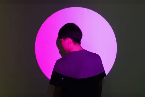 A person stands in front of a bright pink circular light, creating a striking silhouette effect.